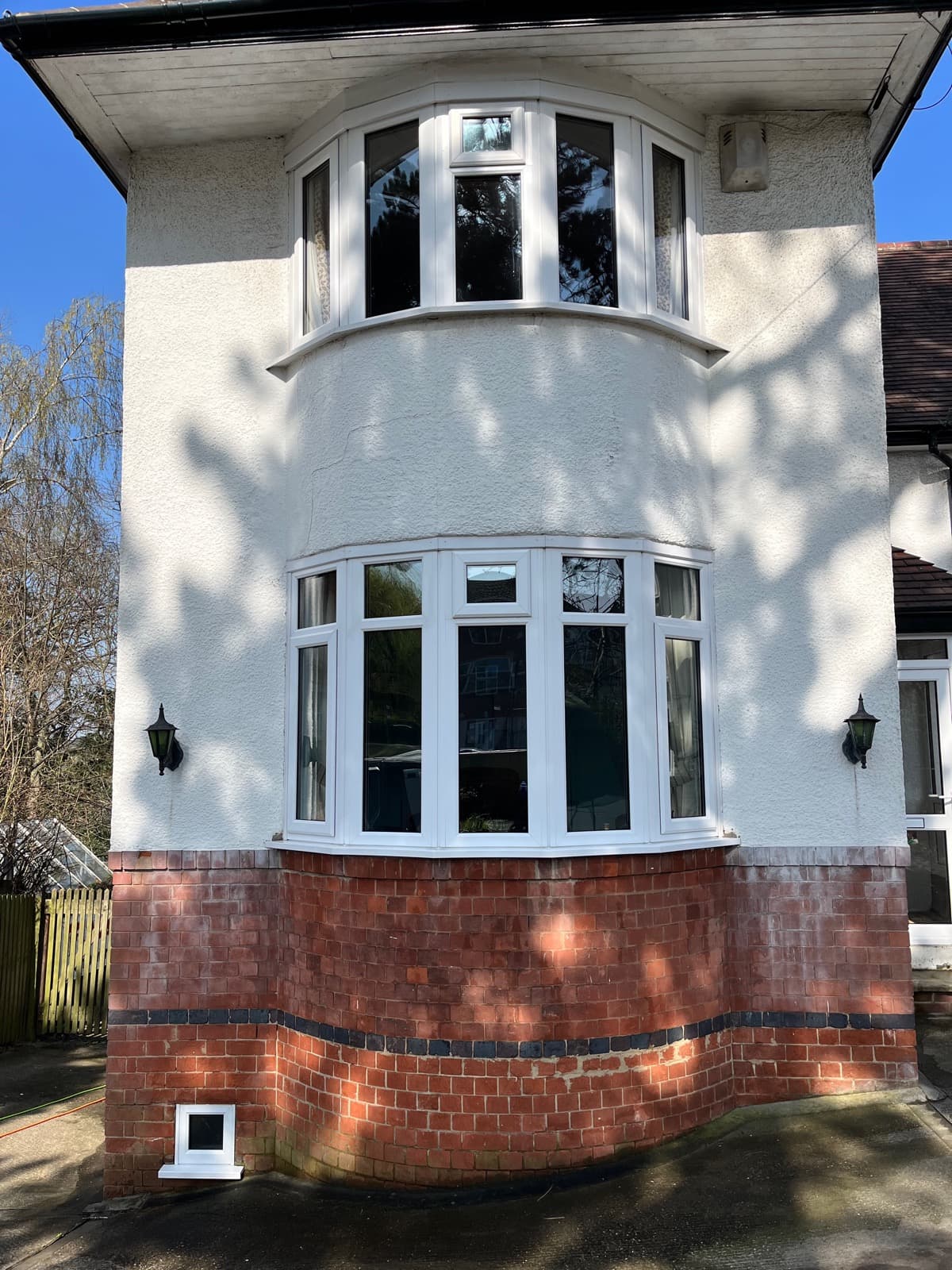 Period property bay window with white render and brick base — freshly cleaned glass with dappled sunlight