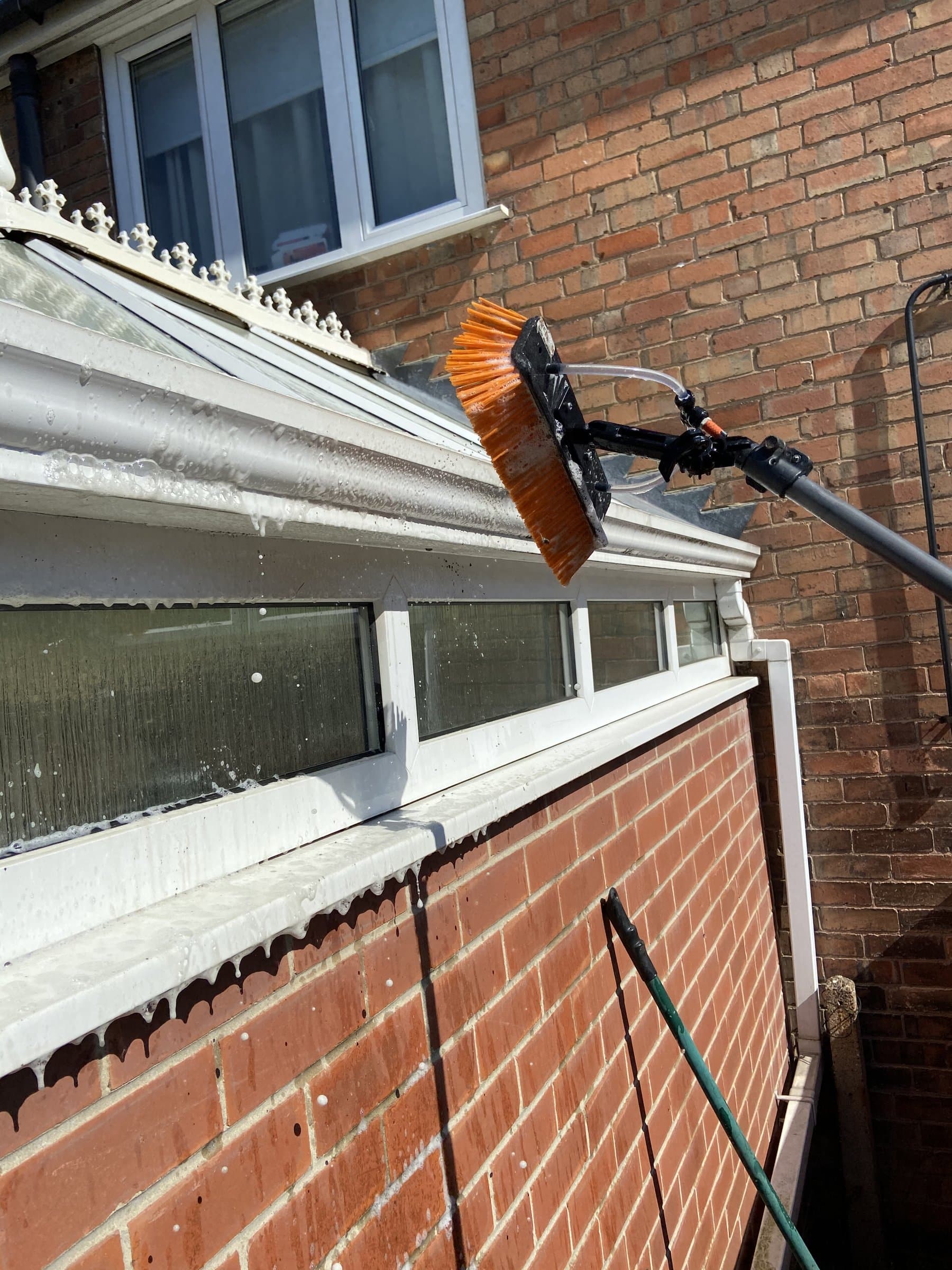 Water-fed pole cleaning a conservatory roof from the ground, working the solution down the glass