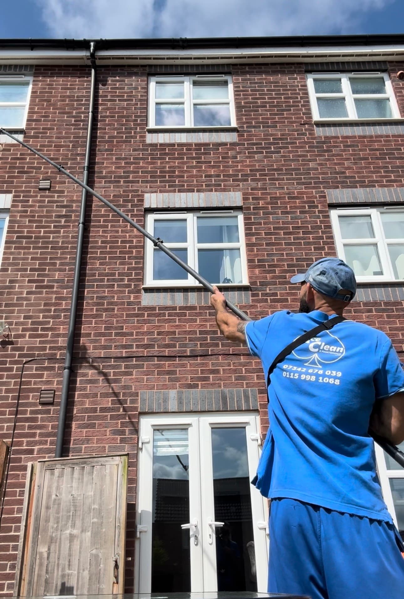 Ace Exterior operator in branded uniform cleaning the upper windows of a townhouse with a water-fed pole